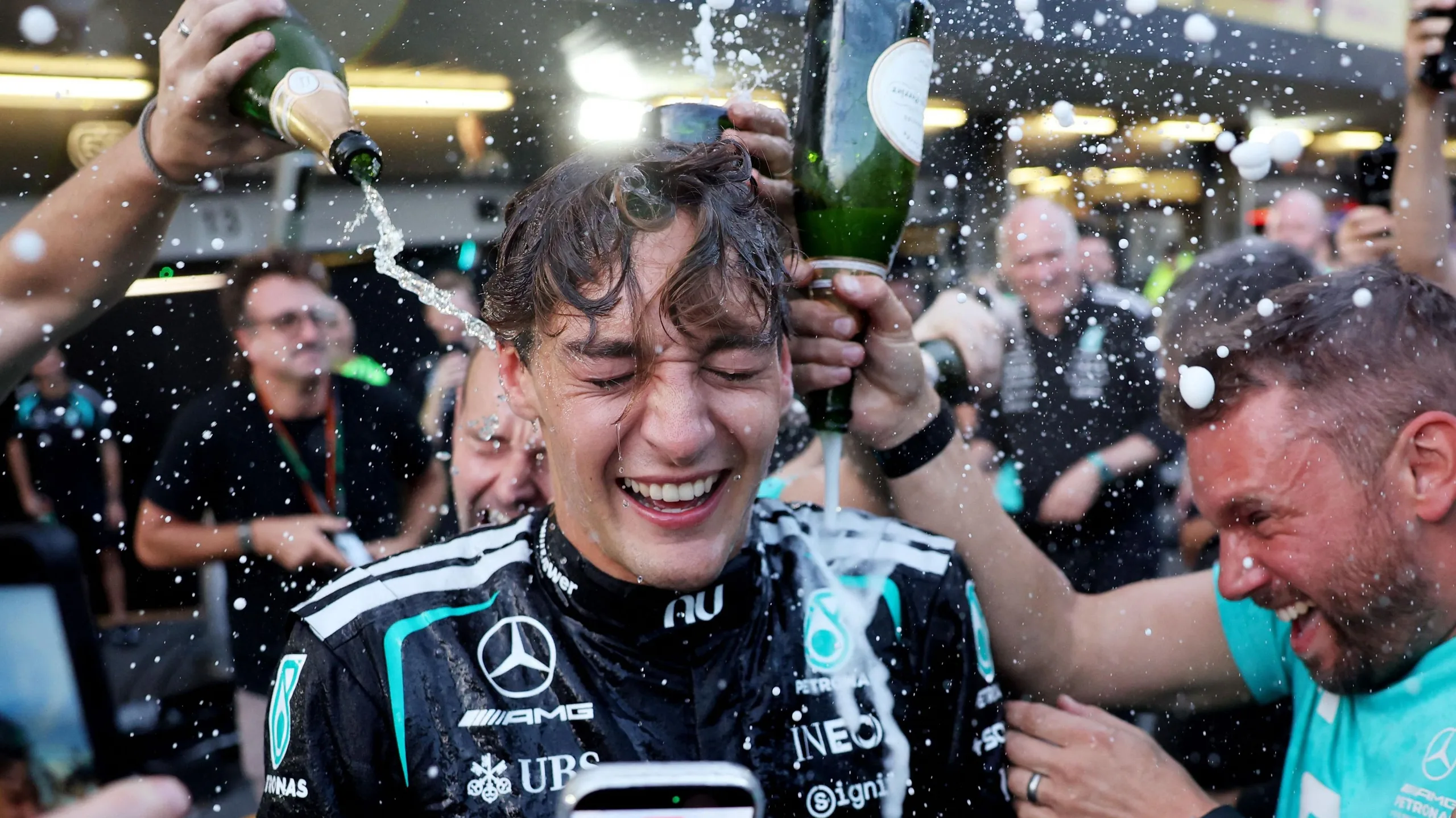 George Russell celebrating with Mercedes team members pouring champagne over him