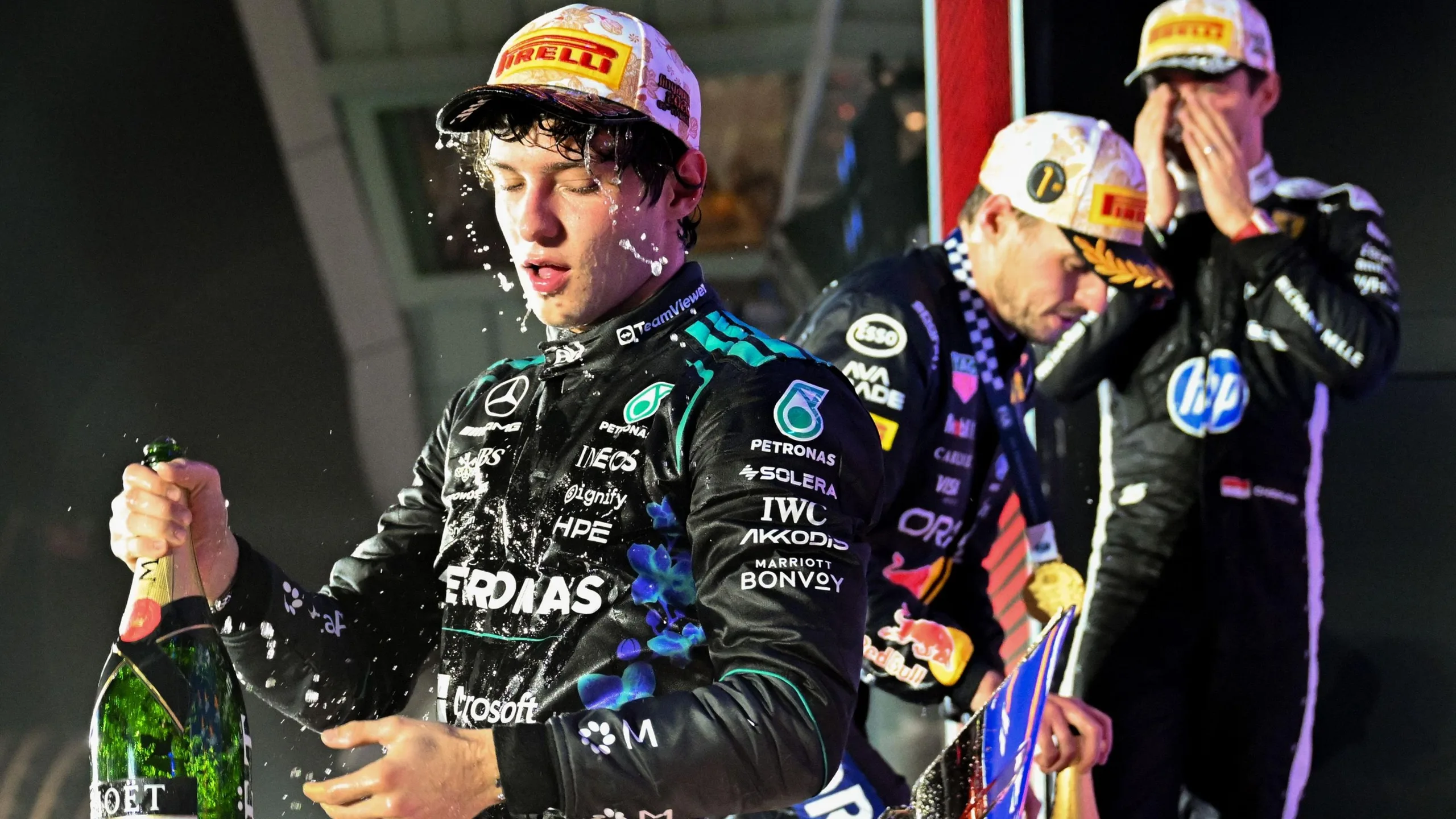 Mercedes driver Kimi Antonelli covered in champagne with Max Verstappen and Charles behind him on the podium after the Singapore Grand Prix