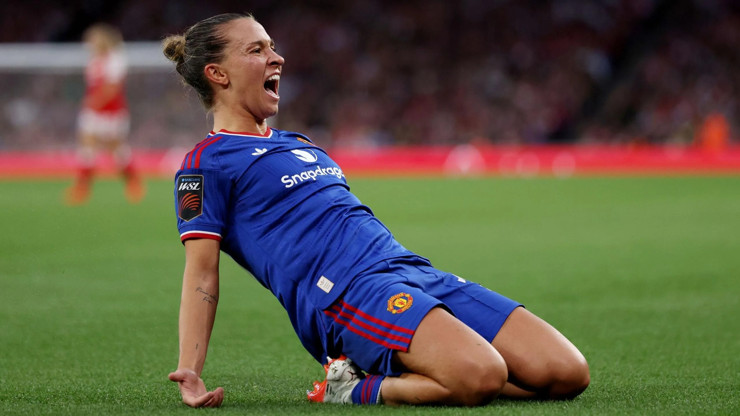 Julia Zigiotti, in blue kit, slides on her knees to celebrate her opening goal for Manchester United at Arsenal