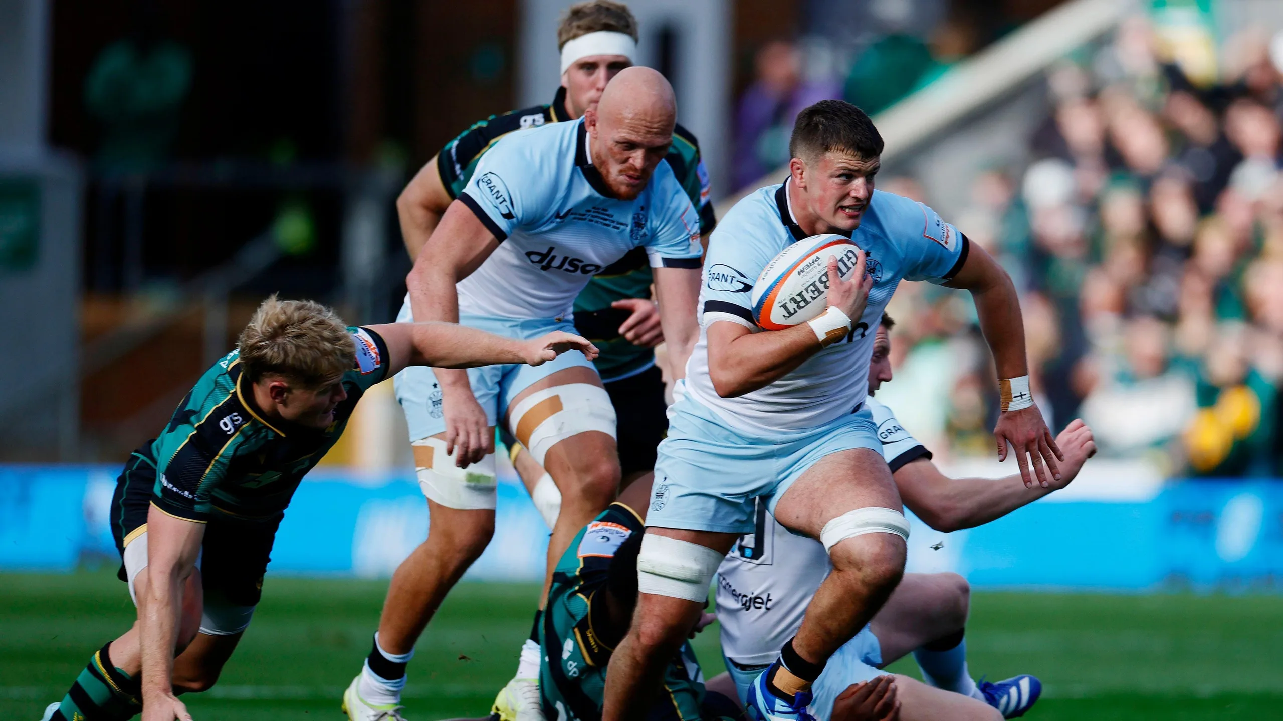 Arthur Green runs with the ball under his right arm as Miles Reid tracks behind him and a Northampton player tries to make a tackle from the floor