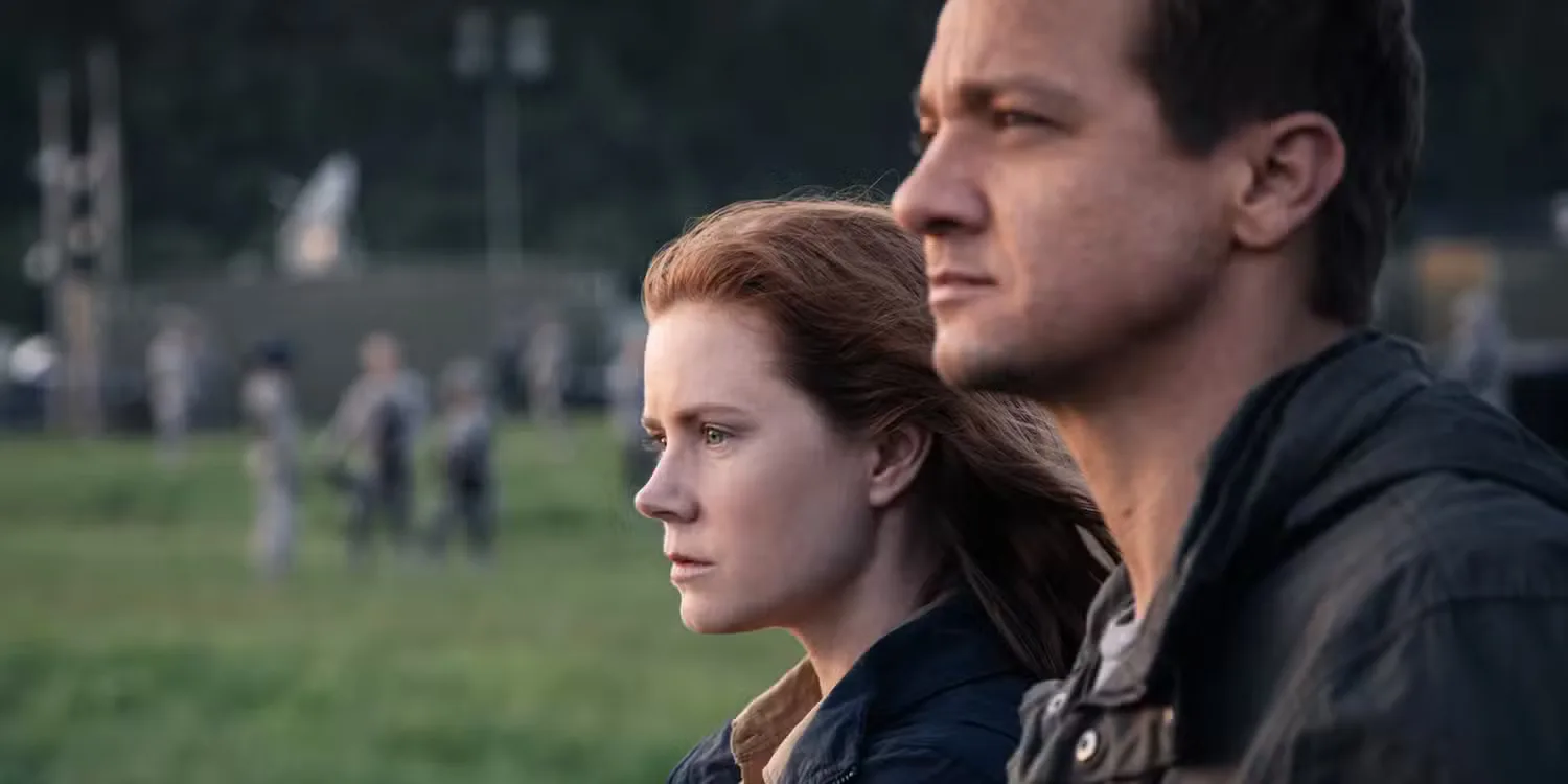 Amy Adams and Jeremy Renner stand side-by-side outdoors and stare ahead in Arrival. 