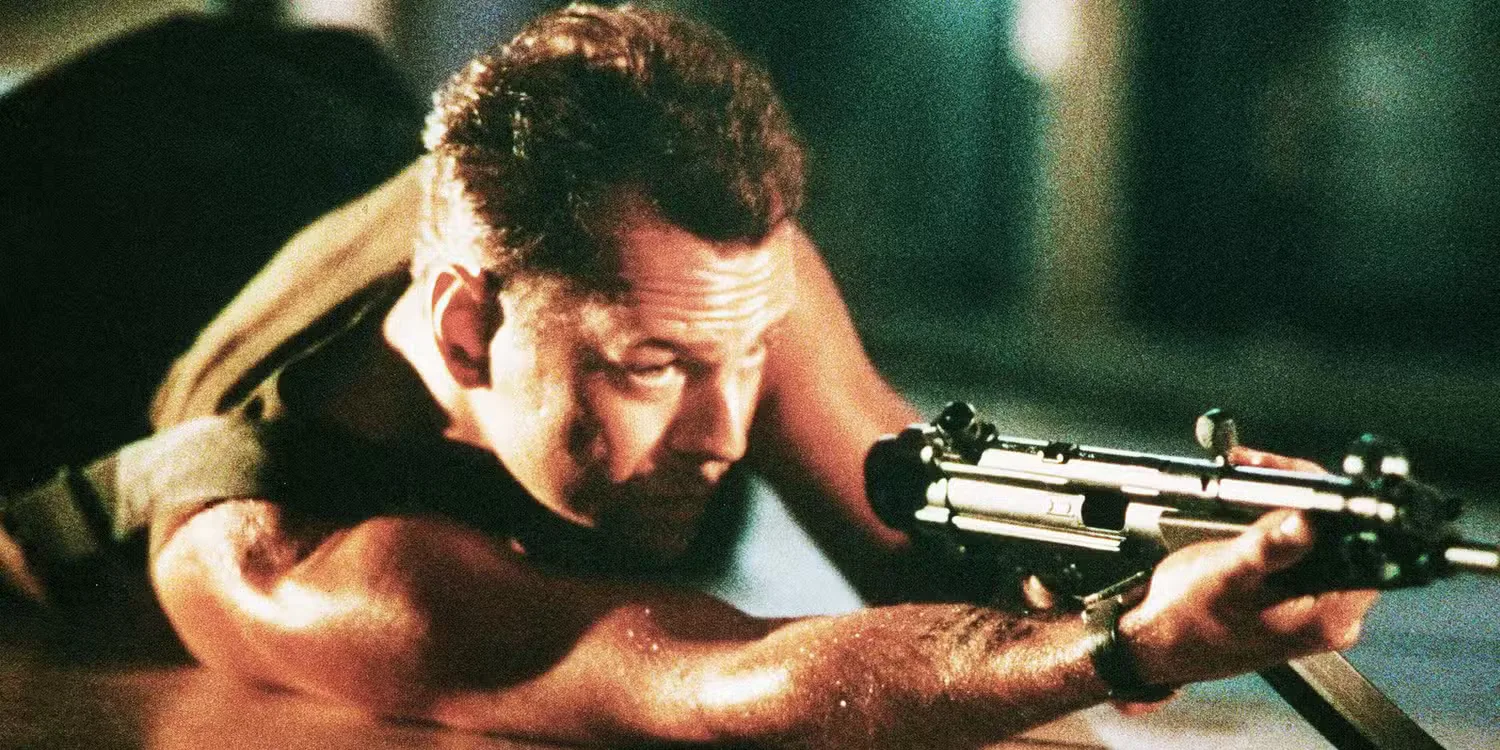 Bruce Willis as John McClane lying on the ground, pointing a gun, in the first Die Hard (1988)