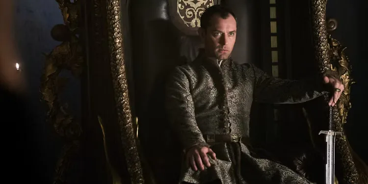 Jude Law as King Vortigern sits on his throne with his hand on his sword as he glares menacingly in 'King Arthur: Legend of the Sword' (2017)
