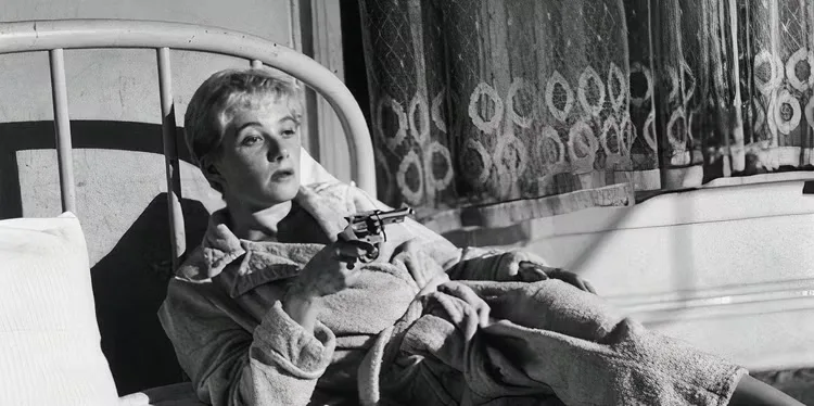 A woman in bed pointing a gun at someone off-camera in 'Kiss Me Deadly'