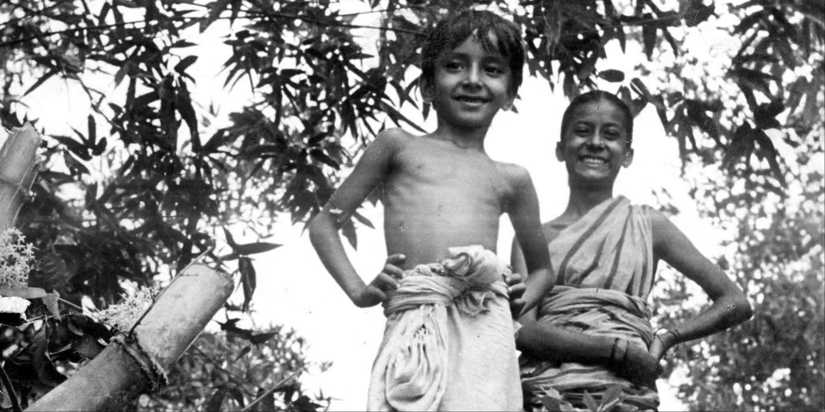 Uma Das Gupta and Subir Banerjee as Durga and Apu standing in a forest smiling in Pather Panchali