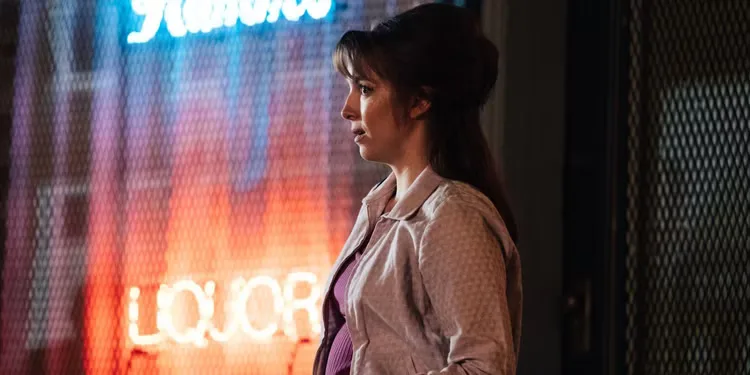Jodie Comer standing outside a liquor store at night as Kathy in The Bikeriders.