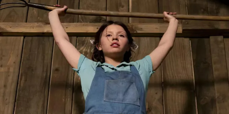Mia Goth as Pearl lifting a pitchfork over her head in Ti West's Pearl