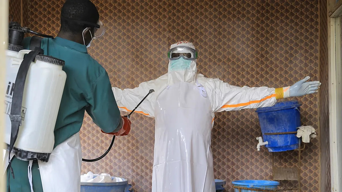 A healthcare worker in protective clothing is disinfected by a colleague inside a treatment center for Ebola patients in Beni, DR Congo.