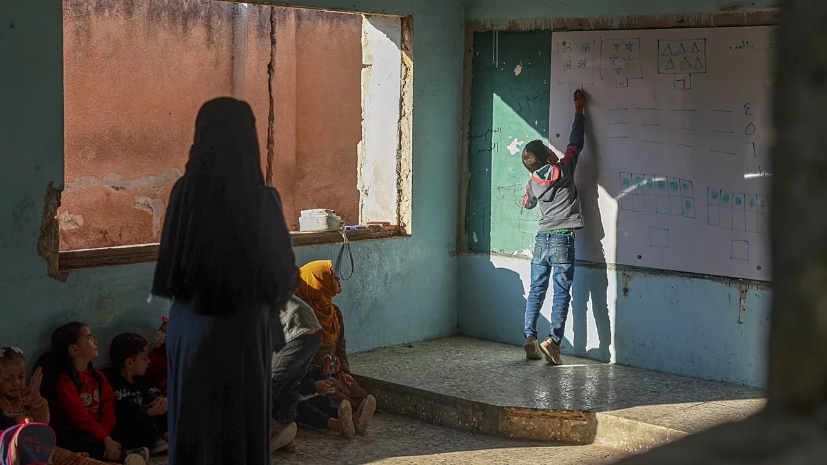 A pupil writes on the whiteboard as classmates and their teacher watch during a lesson at "Maar Shamarin" Primary School, whose walls still bear bullet holes from the war.