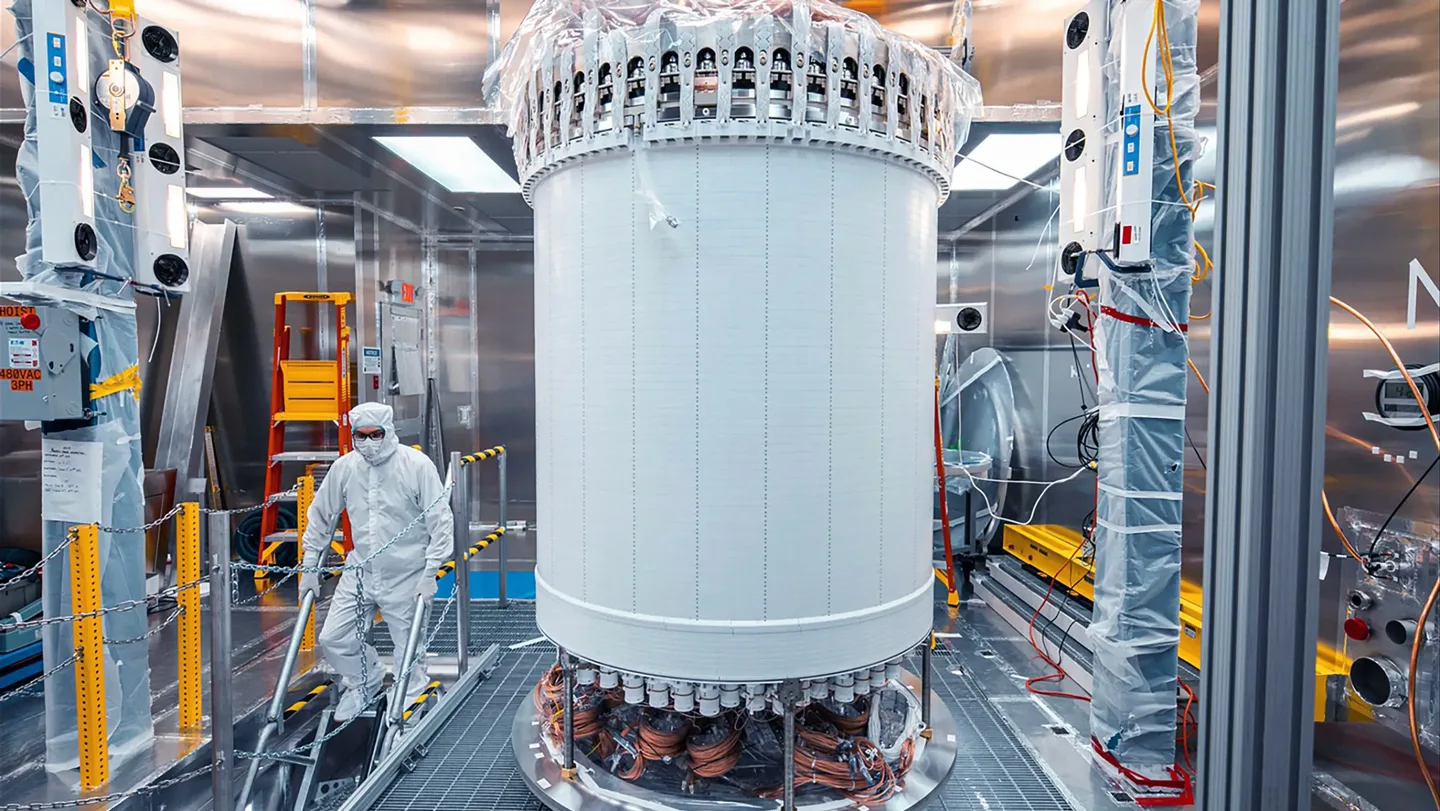 A person stands next to a large cylindrical piece of the LZ detector